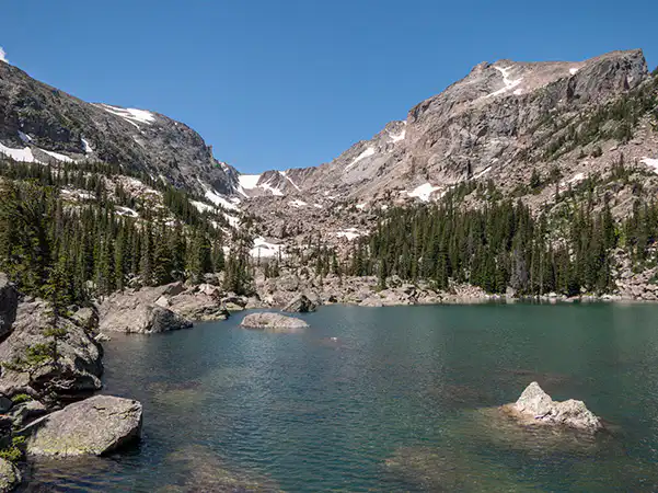 Rocky Mountain National Park lake with trees lining the shoreline and mountains in the background